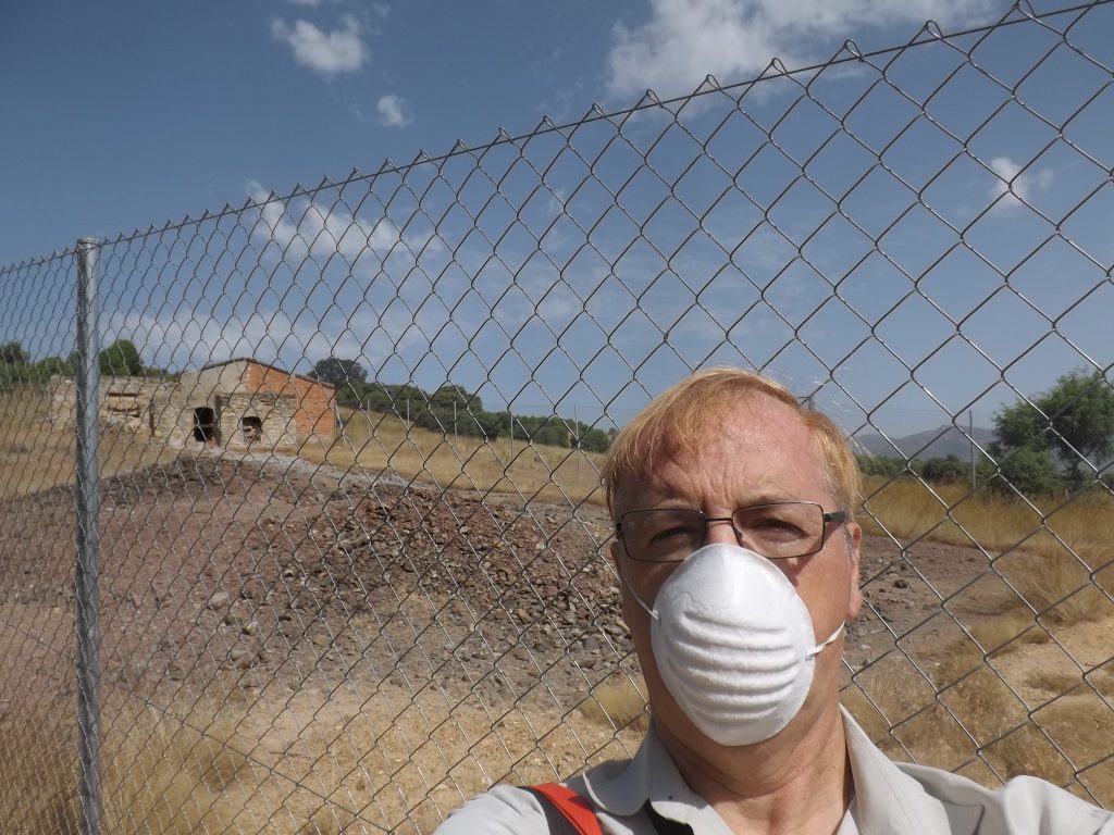 El autor de este reportaje, Pedro Pozas, con mascarilla junto a los residuos de arsénico. Los escombros de tonos grisáceos que se observan detrás son altamente peligrosos por contacto y por vía respiratoria. (Fotografía: Pedro Pozas).